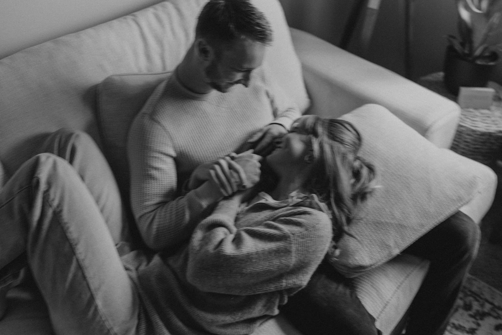 A tender moment of connection and intimacy is captured in this black and white photograph, as a couple shares a quiet moment together on their couch at home.